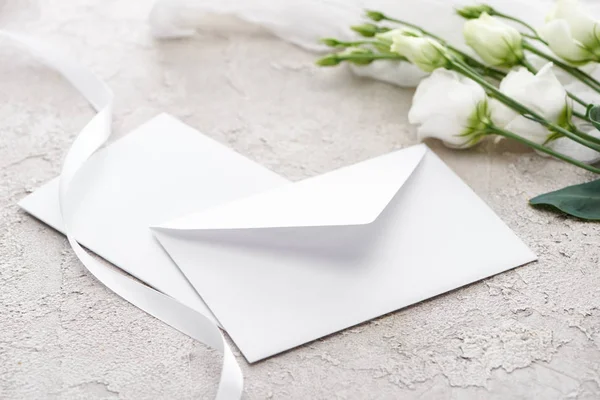 Envelope branco perto de flores eustoma e fita branca na superfície texturizada cinza — Fotografia de Stock