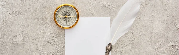 Panoramic shot of quill pen on white card near golden compass on grey textured surface — Stock Photo