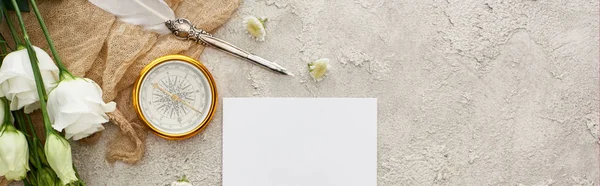 Panoramic shot of quill pen on beige sackcloth near white card, golden compass and eustoma flowers on grey textured surface — Stock Photo