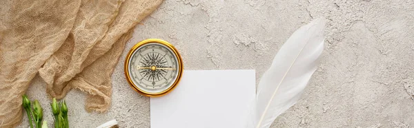 Panoramic shot of quill pen on piece of paper near beige sackcloth and golden compass on grey textured surface — Stock Photo