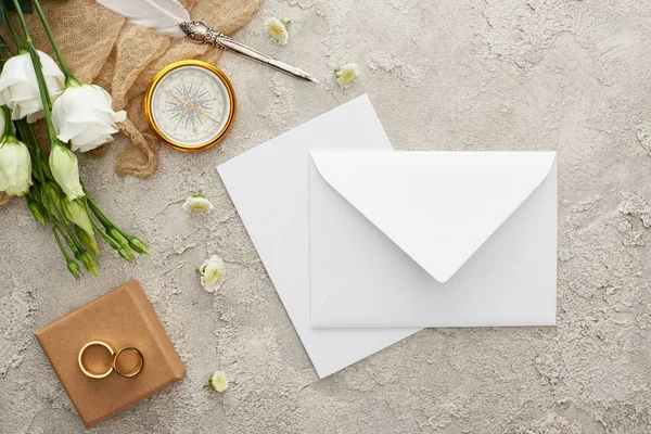 Draufsicht auf weißen Umschlag, Kompass, Trauringe auf Geschenkbox auf grau strukturierter Oberfläche — Stockfoto