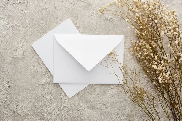 Vue de dessus du morceau d'enveloppe blanche et carte près des fleurs sur la surface texturée — Photo de stock