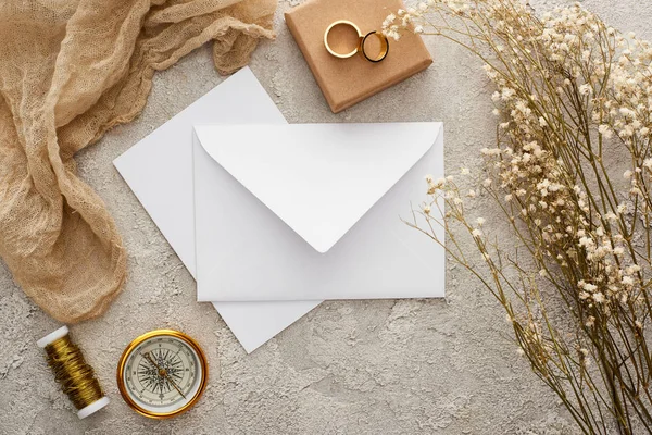 Vista superior do envelope perto de pano de saco bege, bússola dourada e anéis de casamento na superfície texturizada — Fotografia de Stock