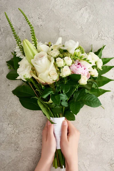 Abgeschnittene Ansicht einer Frau mit Blumenstrauß auf grau strukturierter Oberfläche — Stockfoto