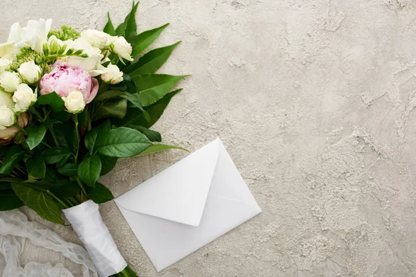 Top view of bouquet of flowers near white envelope on textured surface — Stock Photo