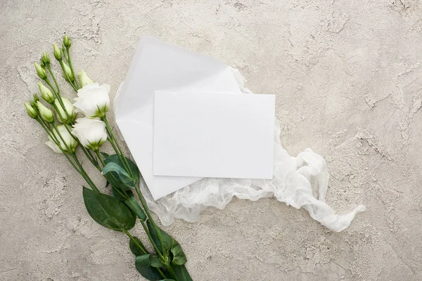 Top view of blank white card on white cheesecloth near eustoma flowers on textured surface — Stock Photo