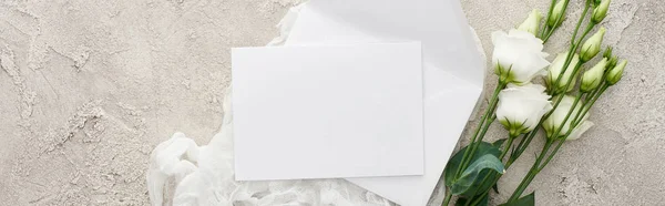 Panoramic shot of empty invitation card on white cheesecloth near eustoma flowers on textured surface — Stock Photo