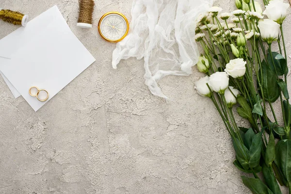 Vista superior de anéis de casamento no cartão de convite em branco, toalha de queijo branca e flores na superfície texturizada — Fotografia de Stock