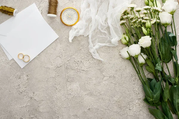 Top view of wedding rings on blank invitation card, white cheesecloth and flowers on textured surface — Stock Photo