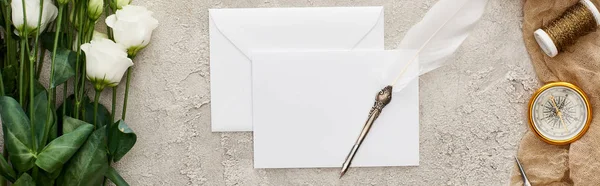 Panoramic shot of quill pen on empty card, eustoma flowers, compass and spool on beige sackcloth on textured surface — Stock Photo