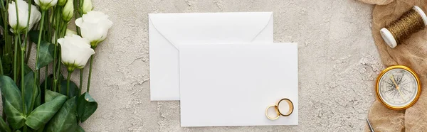 Panoramic shot of golden rings on empty card, eustoma flowers, compass and bobbin on beige sackcloth on textured surface — Stock Photo