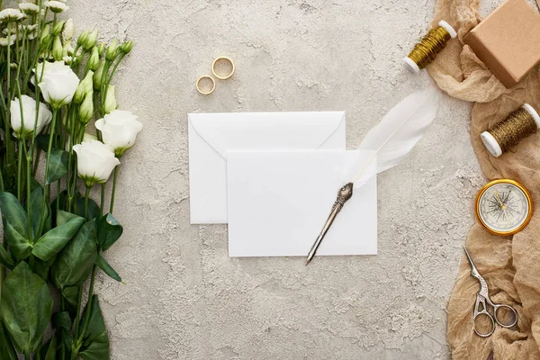 Vista dall'alto della penna a penna su carta vuota, fiori di eustoma, fedi nuziali, confezione regalo, bussola, forbici e bobine su sacco beige su superficie strutturata — Foto stock