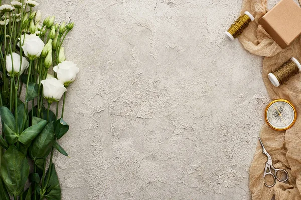 Vue de dessus des fleurs d'eustomes près de la boîte cadeau, boussole, ciseaux et bobines sur sac beige sur surface texturée — Photo de stock