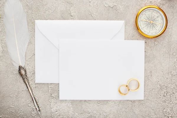 Vue du dessus des alliances et du stylo plume sur carte blanche vierge et boussole dorée sur surface texturée — Photo de stock