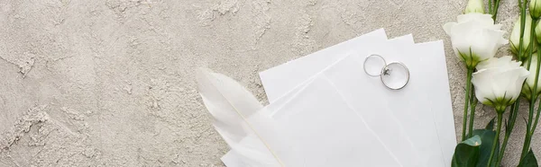 Panoramic shot of silver rings on invitation cards near white eustoma flowers on textured surface — Stock Photo