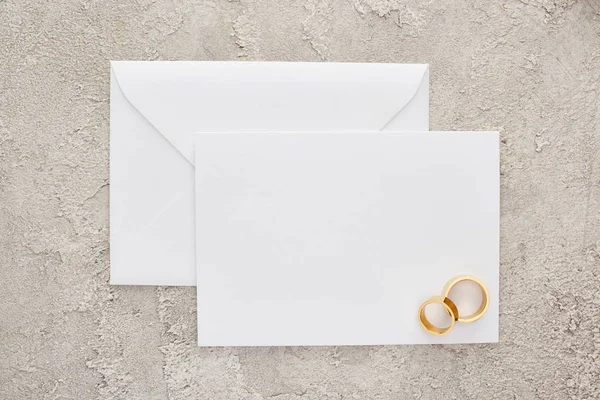 Vista superior de anillos de boda dorados en la tarjeta de invitación en blanco en la superficie texturizada - foto de stock