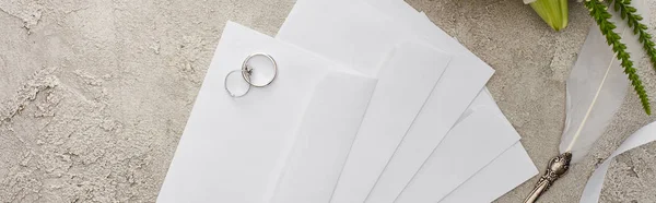 Panoramic shot of wedding rings on envelopes near quill pen on textured surface — Stock Photo