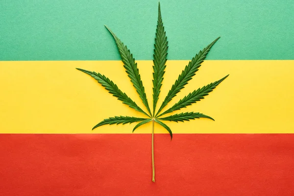 Vue du dessus de la feuille de cannabis sur fond de drapeau rastafarien — Photo de stock