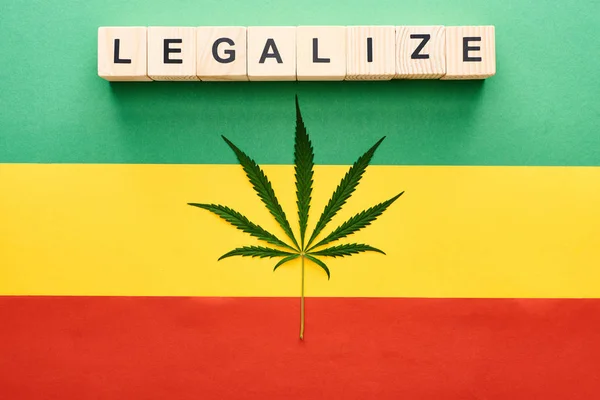 Vista superior de la hoja de cannabis y bloques de madera con letras legalizadas en el fondo de la bandera rastafari - foto de stock