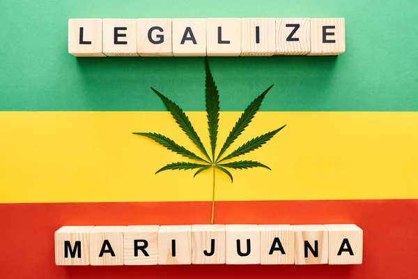 Top view of cannabis leaf and wooden blocks with legalize marijuana lettering on Rastafarian flag background — Stock Photo