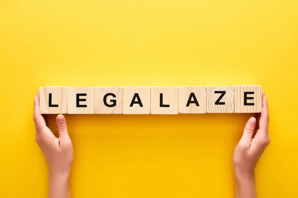 Cropped view of woman holding wooden blocks with legalize lettering on yellow background — Stock Photo