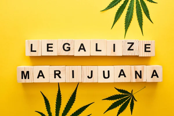Vue du dessus des feuilles de cannabis et des blocs de bois avec légaliser le lettrage de marijuana sur fond jaune — Photo de stock