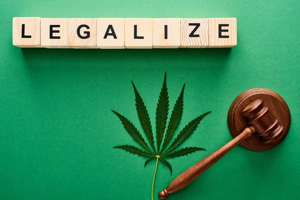 Vista superior de las hojas de cannabis verde y legalizar la palabra en cubos de madera cerca del mazo sobre fondo verde - foto de stock