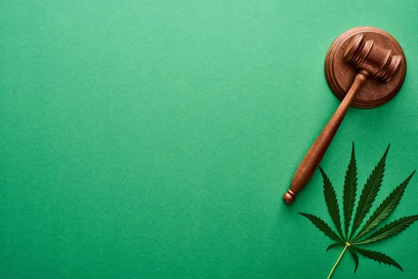 Top view of green cannabis leaf near wooden gavel on green background with copy space — Stock Photo
