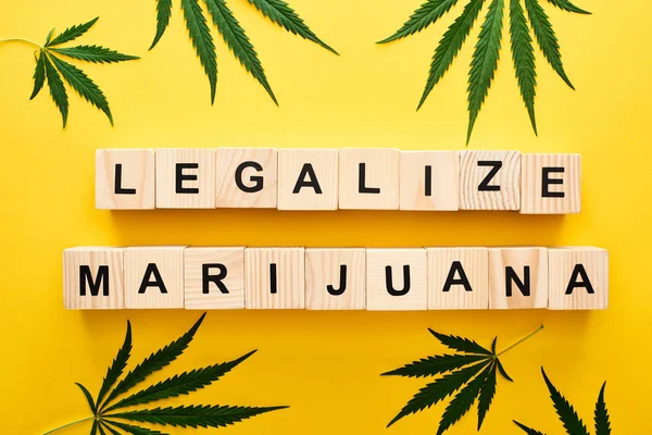Vista dall'alto di foglie di cannabis e blocchi di legno con legalizzare le parole di marijuana su sfondo giallo — Foto stock