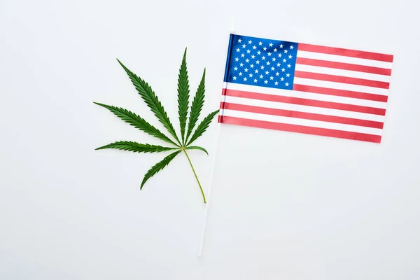 Vista superior de la hoja de cannabis verde cerca de la bandera americana sobre fondo blanco - foto de stock