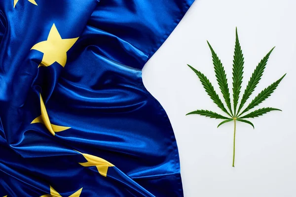 Vue du dessus de la feuille de cannabis verte près du drapeau de l'Europe sur fond blanc — Photo de stock