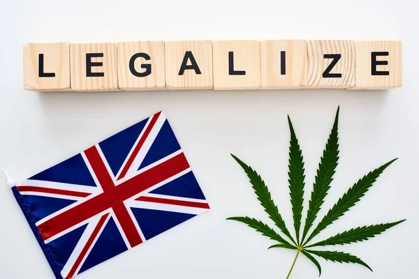 Vista superior de la hoja de cannabis y legalizar las letras en cubos de madera cerca de la bandera de Gran Bretaña sobre fondo blanco - foto de stock