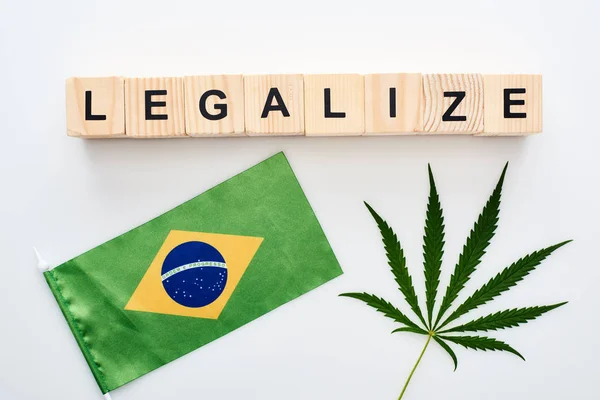 Top view of green cannabis leaf and legalize lettering on wooden cubes near flag of Brazil on white background — Stock Photo