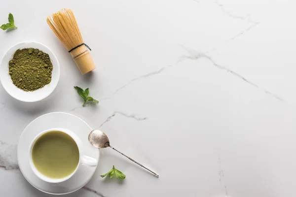 Ansicht von grünem Matcha-Tee mit Schneebesen auf weißem Tisch — Stockfoto