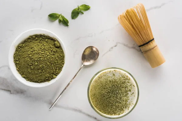 Vista superior de polvo de té matcha verde y beber en vidrio sobre mesa blanca - foto de stock