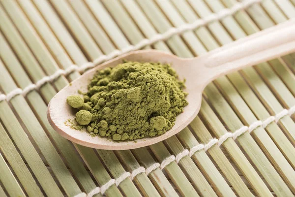 Cuillère en bois avec poudre de thé matcha vert sur tapis de bambou — Photo de stock