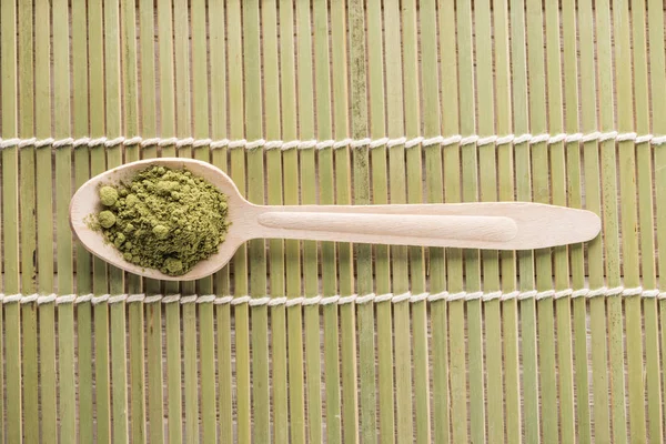 Vue de dessus de cuillère en bois avec poudre de thé matcha vert sur tapis de bambou — Photo de stock