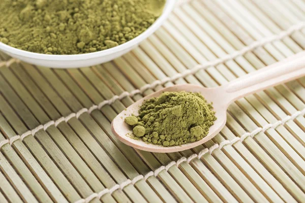 Bowl and wooden spoon with powder of green matcha tea on bamboo mat — Stock Photo