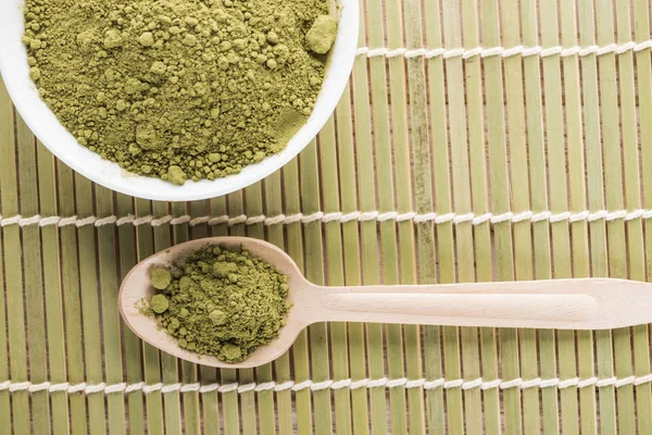 Top view of wooden spoon with powder of green matcha tea on bamboo mat — Stock Photo