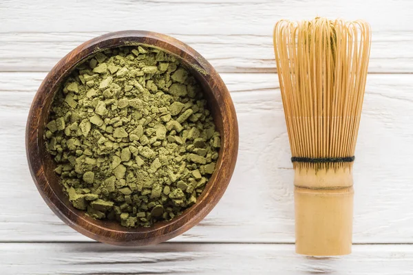 Top view of wooden bowl with powder of green matcha tea on white table with whisk — Stock Photo