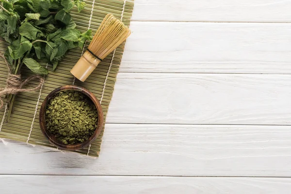 Vista dall'alto del tè verde matcha in polvere e menta sul tappetino di bambù sul tavolo bianco — Foto stock