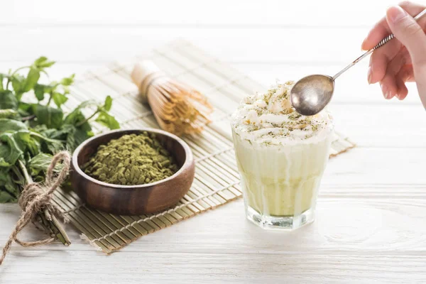 Cropped view of woman with matcha matcha tea in glass with whipped cream — Stock Photo