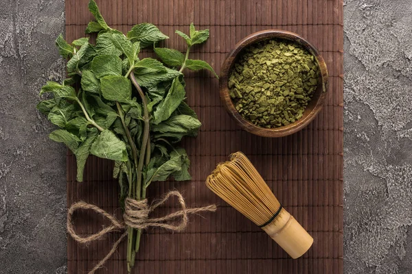 Vista dall'alto del tè verde matcha in polvere, menta e frusta su tappetino di bambù sul tavolo di pietra scura — Foto stock