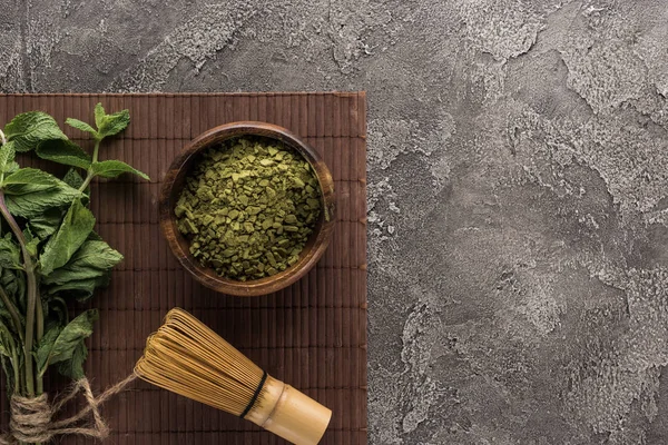 Blick von oben auf grünen Matcha-Tee mit Minze und Schneebesen auf Bambusmatte auf dunklem Steintisch — Stockfoto