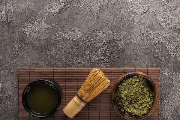 Vista superior del té matcha verde con batidor en la estera de bambú en la mesa de piedra oscura - foto de stock