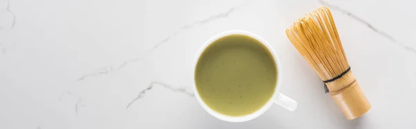 Ansicht von grünem Matcha-Tee mit Schneebesen auf weißem Tisch — Stockfoto