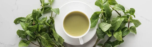 Acostado plano con taza de té matcha verde con menta sobre mesa blanca - foto de stock