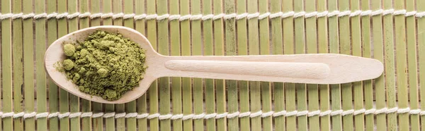 Top view of wooden spoon with powder of green matcha tea on bamboo mat — Stock Photo