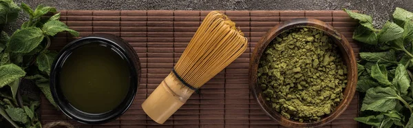 Vista superior do pó de chá matcha verde com hortelã e batedor no tapete de bambu na mesa de pedra escura — Fotografia de Stock