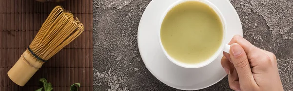 Vista ritagliata della donna che tiene il tè matcha matcha sul tavolo con frusta — Foto stock